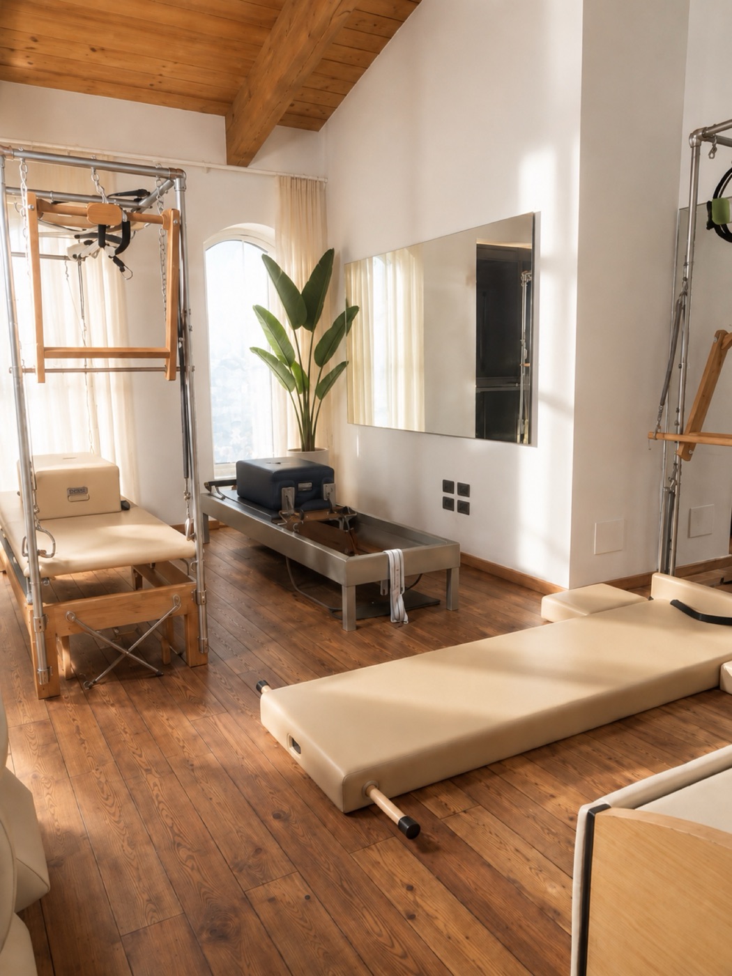Vista d'insieme dello studio Pilates di Grosseto: travi a vista, Cadillac e Reformer Gratz, finestra ad arco, pavimento in legno